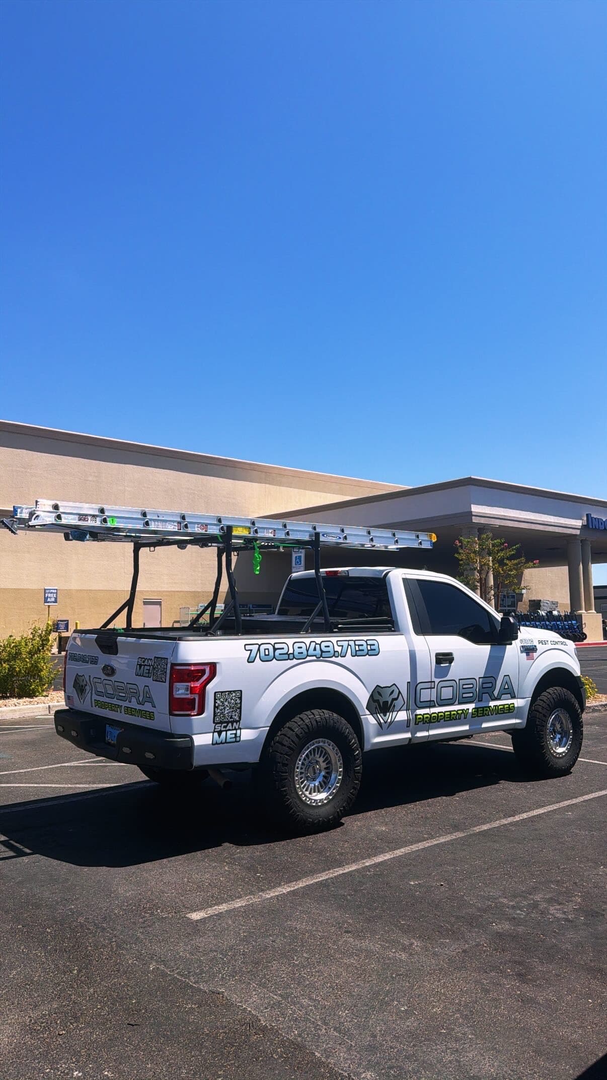 White Cobra Property Services truck with a ladder rack parked under a clear blue sky.